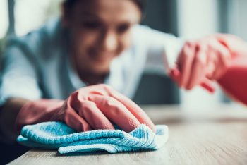 close-up of a woman wearing rubber gloves, cleaning a table with a cloth