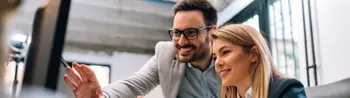 a woman and a man pointing to a desktop monitor in an office environment
