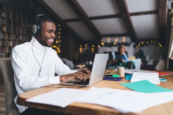 man writing in front of laptop with headphones on