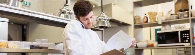 Chef in a kitchen looking at a clipboard of information