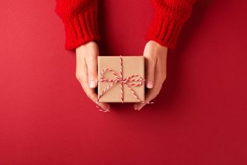 close-up of a pair of hands holding a small gift with a bow, against a red background
