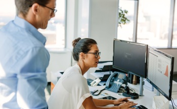 Lady on a computer with a male colleague watching.