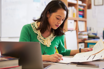 young woman in a green shirt sitting at a desk and taking notes on a paper