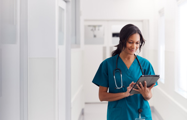 A black woman looking at a tablet in her nursing uniform 