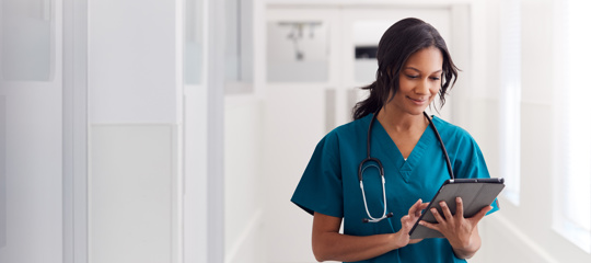 A black woman looking at a tablet in her nursing uniform 