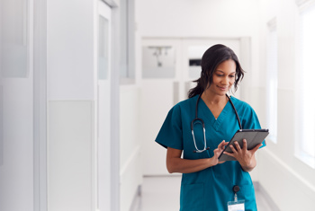 A member of healthcare staff walking down a corridor on a tablet
