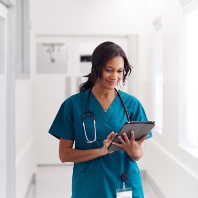 A black woman looking at a tablet in her nursing uniform