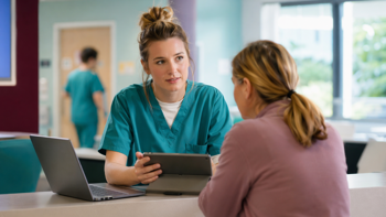 An ED nurse in conversation with a patient whilst using AI-powered healthcare software on her tablet device.