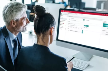 Two professionals collaborating at a computer displaying a red-and-white business software interface