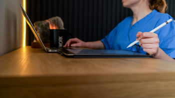 Care worker sitting at a desk, in front of a laptop, with a tablet beside her and stylus in hand