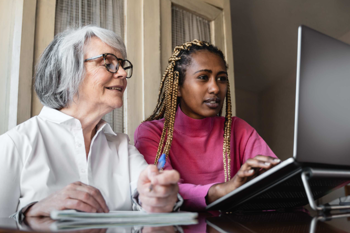 two women, one older than the other, sitting in front of the laptop and taking notes