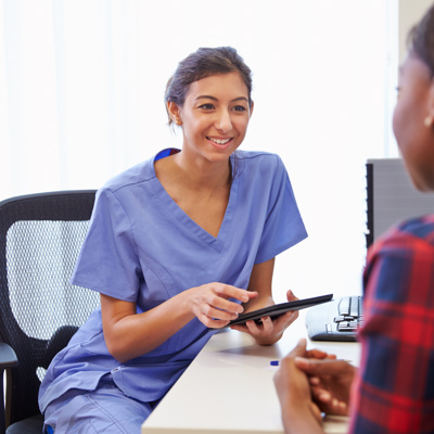 A nurse holding an electronic tablet talking to another woman