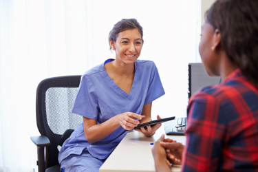 A nurse holding an electronic tablet talking to another woman