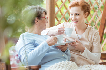 elderly lady and a care worker sitting together in a garden while having a cup of tea