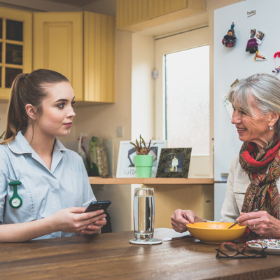 A female nurse in her uniform sitting with an elderly woman