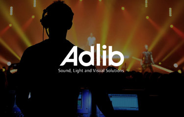 Silhouetted technician at a control panel during a live event, with ‘Adlib Sound, Light and Visual Solutions’ logo