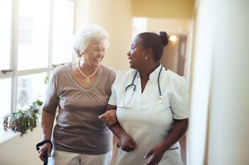 a healthcare worker and an elderly lady walking down the hallway in a care home