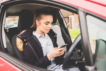 A young lady in her nursing uniform using her phone in her car