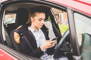 A young lady in her nursing uniform using her phone in her car