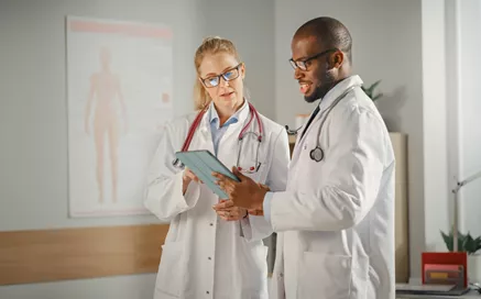 A female doctor showing something on a tablet to a male doctor