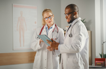 A female doctor showing something on a tablet to a male doctor