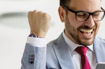 Smiling man in a blue suit celebrating while looking at his smartphone