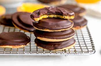 Stack of chocolate-covered cookies on a cooling rack, with one bitten to show orange filling