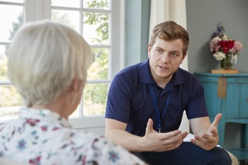 male care worker and elderly resident sitting on a sofa in a care home, having a conversation