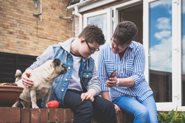 A woman showing something on her phone to a boy who is stroking his dog