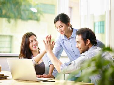 Colleagues around a work desk happy and sharing high fives