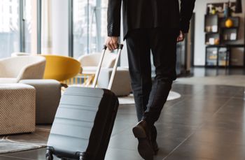 Person pulling a suitcase through a modern lounge with large windows and stylish furniture
