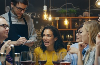 A group of people sitting down in a restaurant smiling whilst a waiter takes their order 