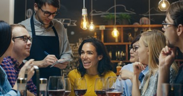 A group of people sitting down in a restaurant smiling whilst a waiter takes their order 