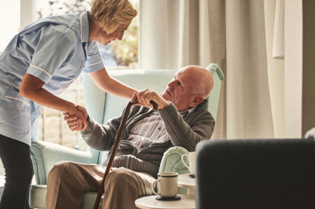 Care worker helping an elderly man with a walking cane stand up.