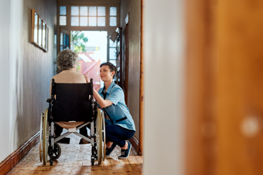 An elderly woman on a wheelchair being comforted by a female nurse