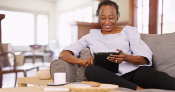 young woman sitting on a couch in her living room, looking at the screen of her tablet
