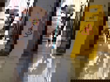 Cleaner tidying bedroom, wet floor sign at the door