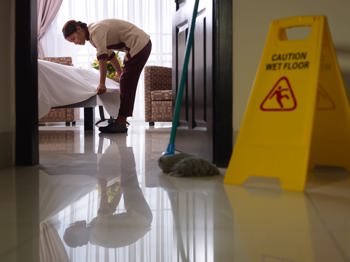 Cleaner tidying bedroom, wet floor sign at the door