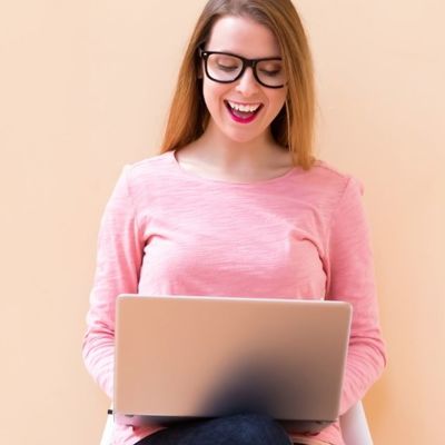 A white woman with glasses on her laptop smiling 