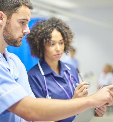 A white male nurse showing something to a black female nurse on a tablet 