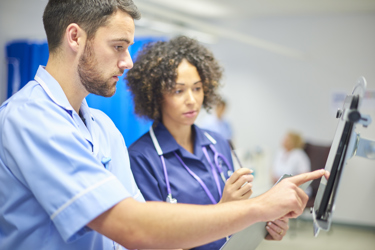 A white male nurse showing something to a black female nurse on a tablet