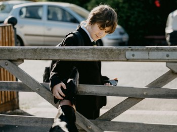 A young boy petting a neighbour's dog on their walk home from school.