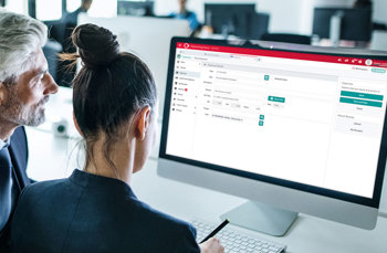  Two professionals collaborating at a computer displaying a red-and-white business software interface