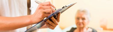A person writing notes with a blurred image of an elderly woman