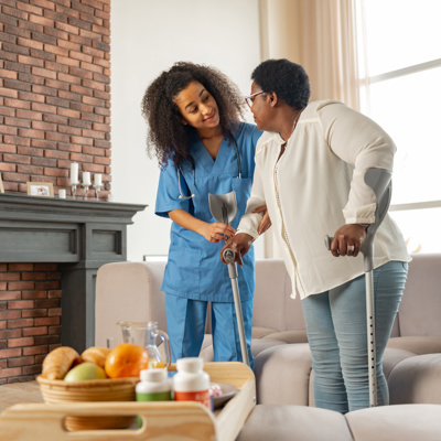 A black female nurse assisting a black woman on crutches to stand up