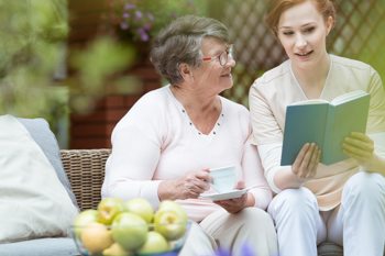 care worker and elderly lady sitting in a garden, looking inside a book