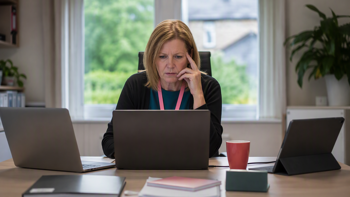 a senior care worker sitting at a desk with multiple devices in front of her, managing multiple care management software platforms