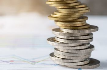 Spiral stack of gold and silver coins in front of a blurred financial chart