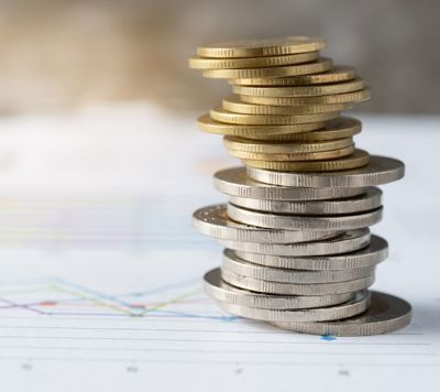  Spiral stack of gold and silver coins in front of a blurred financial chart