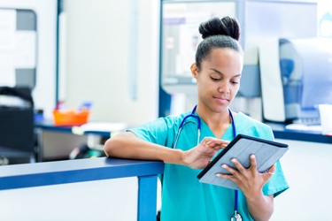 A nurse using smart technology on a digital tablet device whilst working on a hospital ward.